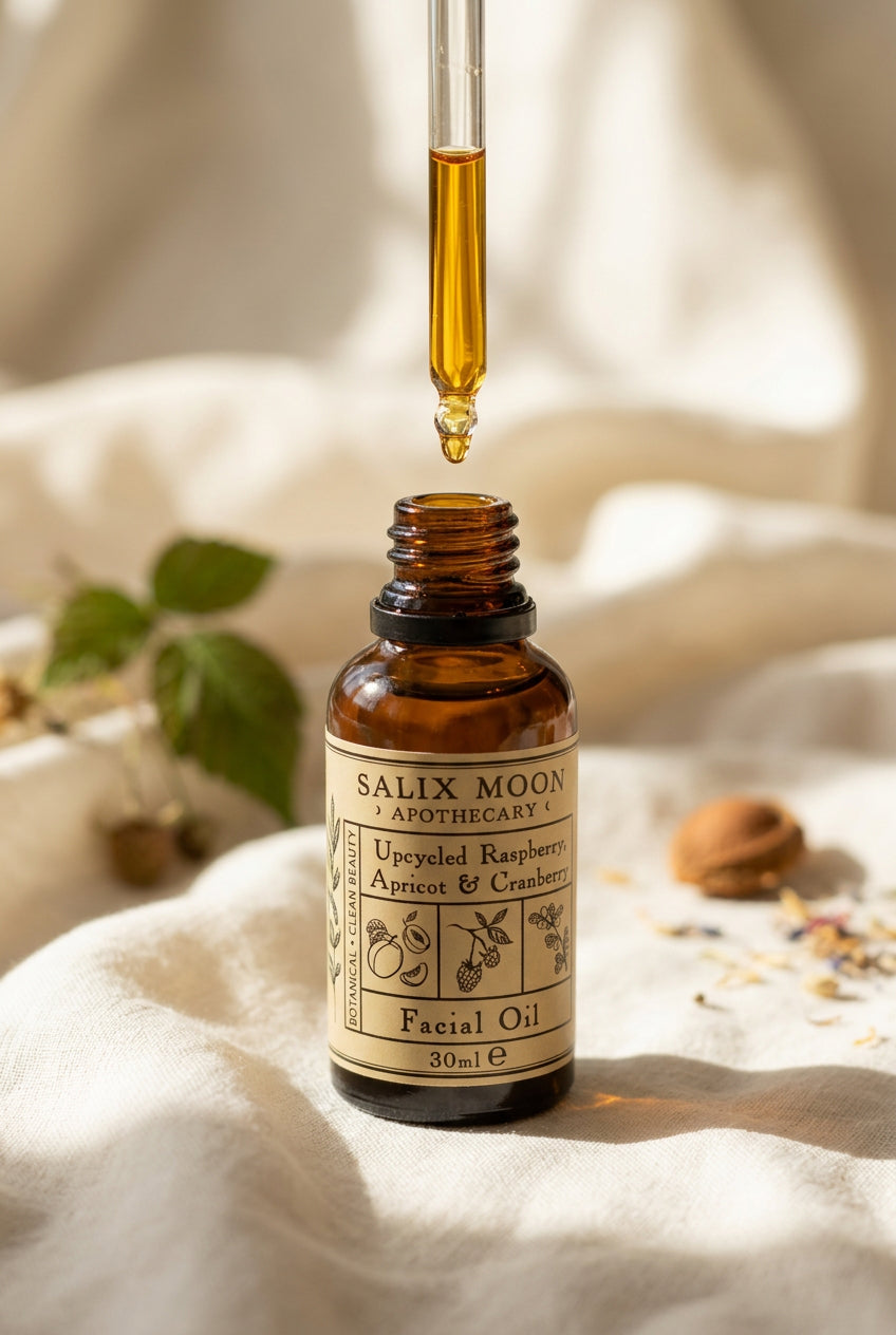 An amber glass dropper bottle of Salix Moon Apothecary Upcycled Raspberry, Apricot & Cranberry Facial Oil, with golden oil dripping from a glass pipette onto a neutral linen background.